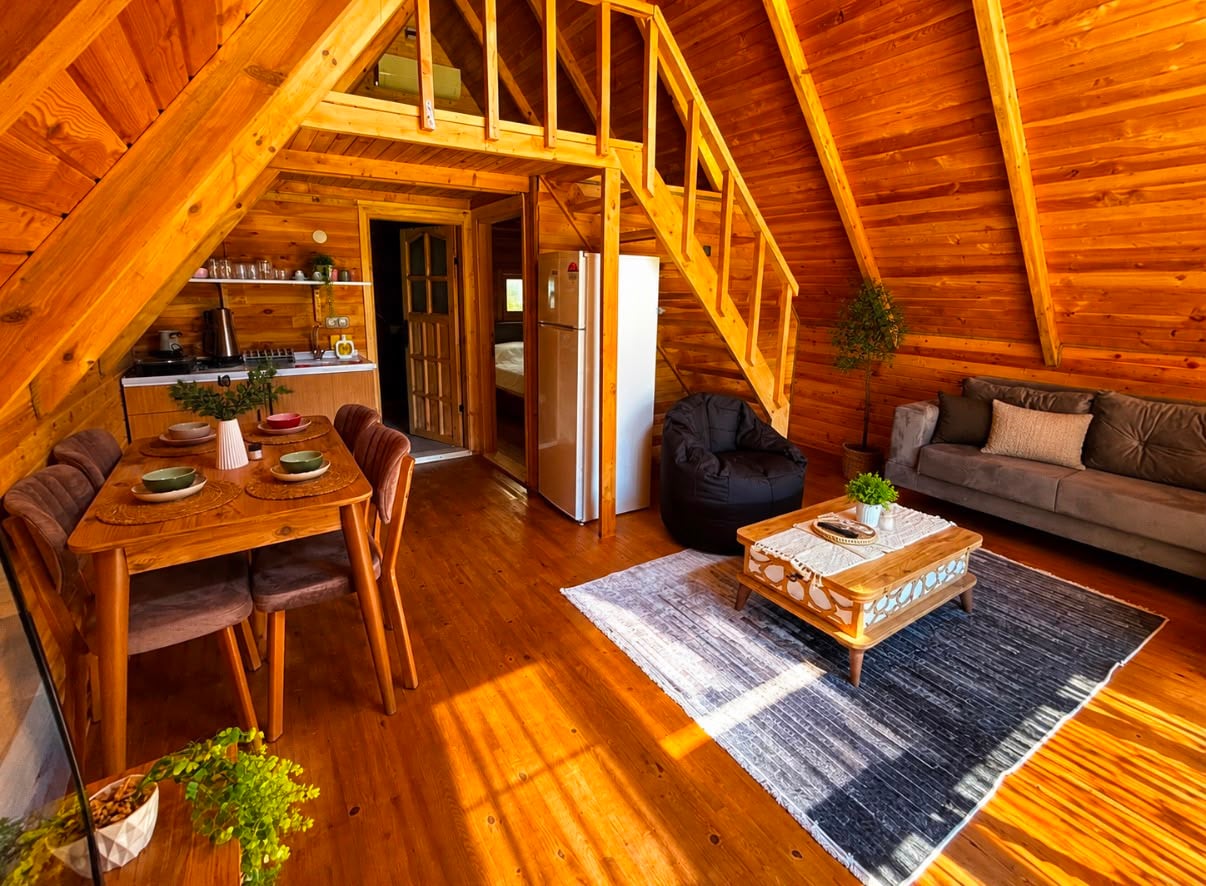 Wide view of the living area showing the dining table, kitchenette and loft staircase in warm pine.