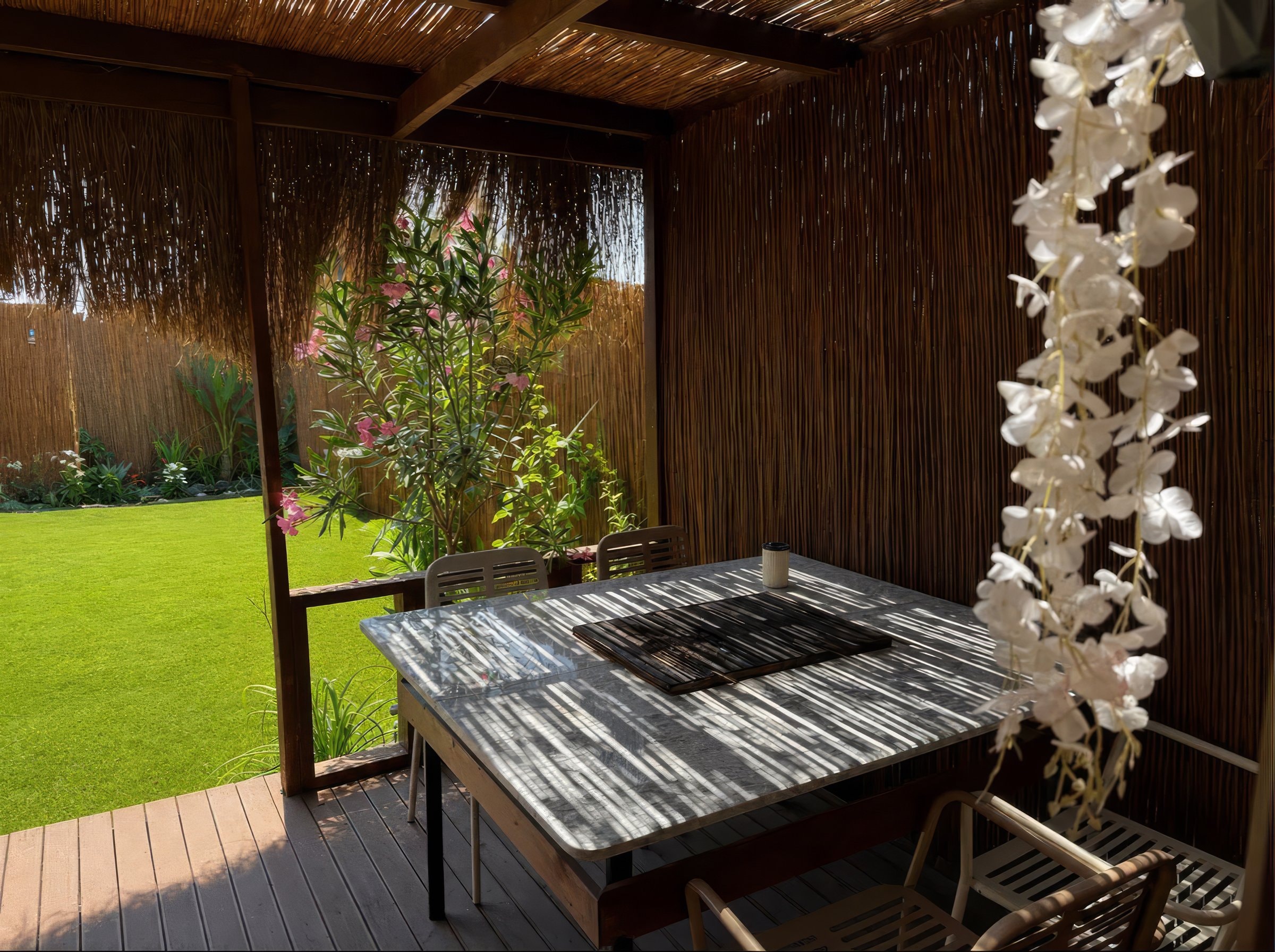 Shaded veranda dining table under a reed roof, looking out onto the private lawn.