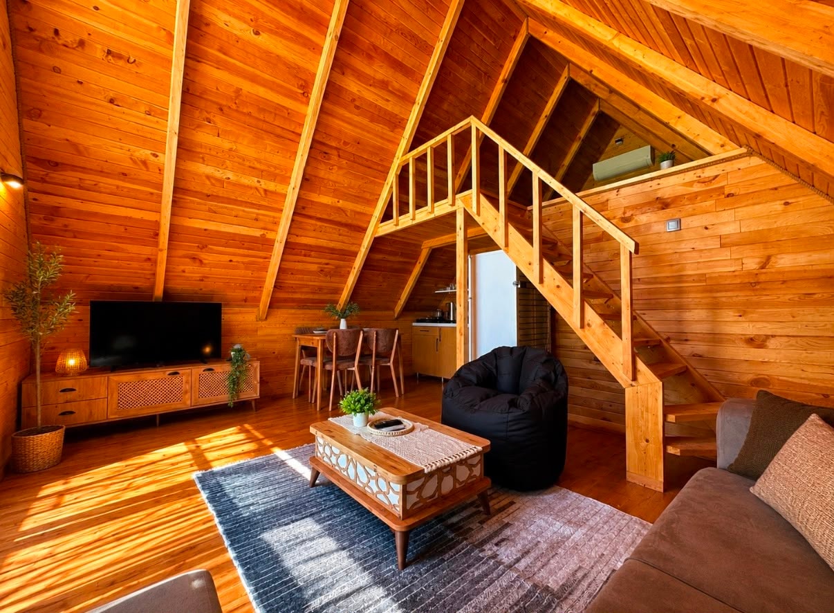 Timber-lined living room with a sofa, television and the staircase leading to the A-frame loft.