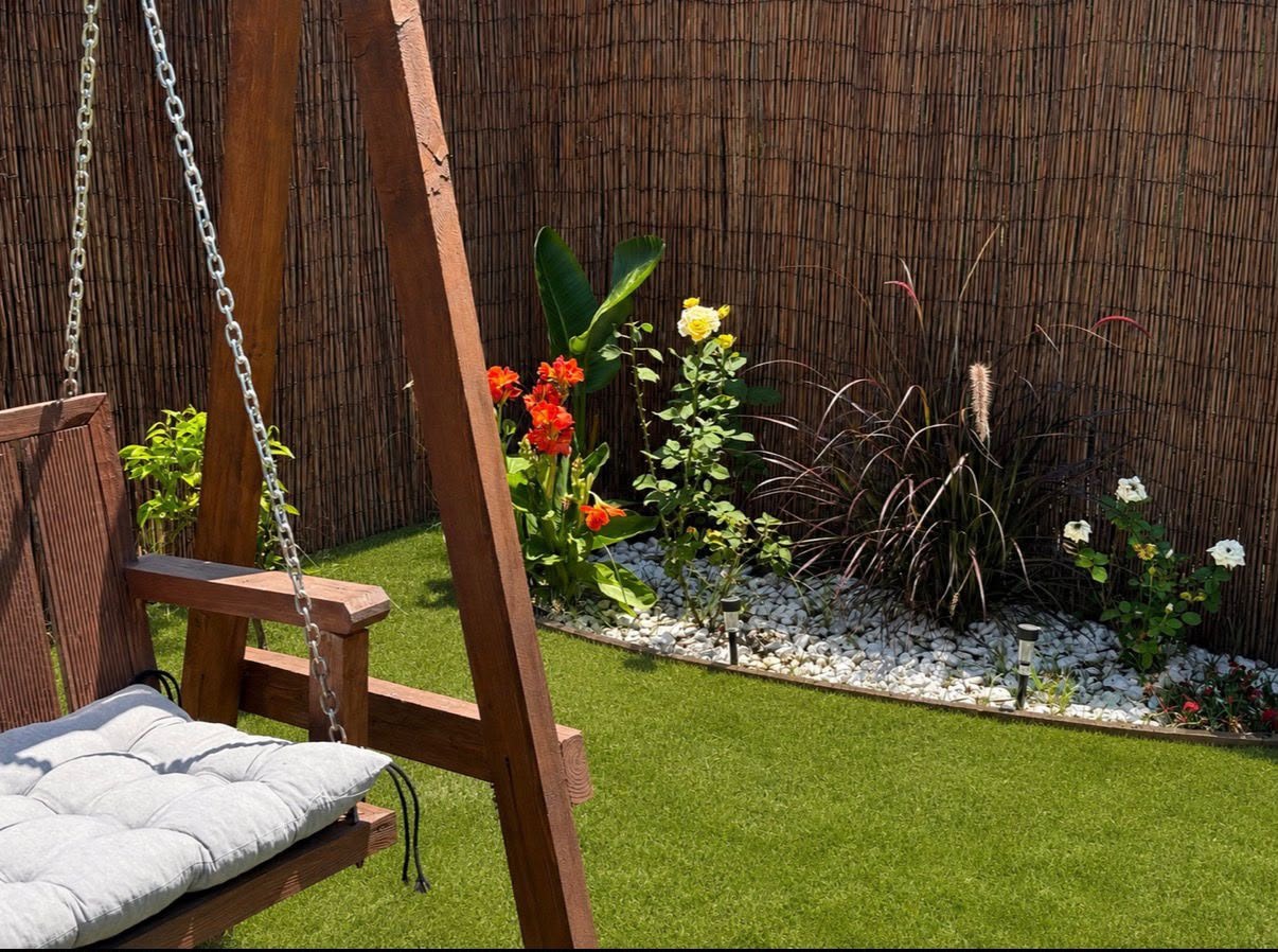 Wooden swing seat with grey cushions beside a planted border of roses, cannas and ornamental grasses.